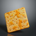 Golden square cracker with small holes and orange spots showing surface texture on gray background