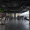 Open Public Office Space With Industrial Ceiling Brick Walls Green Plants Natural Light And Workstations