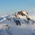 Snowy Mountain Peak With Snow Covered Slopes Rocky Outcrops Under Clear Blue Sky