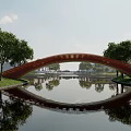 Red Arched Landscape Bridge With Water Reflection Green Grass Trees And Distant Buildings 3d model