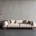 Light Colored Two Seater Sofa With Multiple Pillows Wooden Legs And Twig Decorated Terracotta Pot