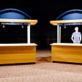 Outdoor Wooden Stalls With Blue Canopies Red Brick Floor And Person Standing At Counter