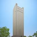 Modern Tall Office Building With Glass Curtain Wall Exterior Against Blue Sky And Green Trees