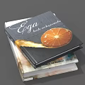 Ega Book With Orange Slice Cover Design Stacked On Other Books