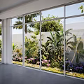 Indoor View Of Outdoor Garden With Diverse Flowering Plants And Tropical Greenery Through Large Glass Windows