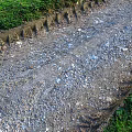Rutted Gravel Ground With Grass Edges Visible Tire Tracks And Loose Stones