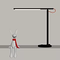 White Rabbit Figurine With Red Scarf And Black Modern Desk Lamp On Light Colored Shelf