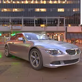Silver BMW Sports Car Parked On Urban Street With Tall Buildings And Evening Lights