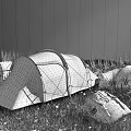 Yellow And Gray Camping Tent Set Up On Green Grassland With Mountain Rocks And Backpacks