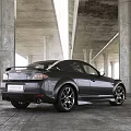 Showroom Interior Displaying Black Sports Car With Concrete Pillars High Ceiling And Bright Lighting