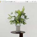 Decorative Ornament Set With White Vase White Flowers Green Leaves On Small Brown Round Table