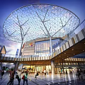 Modern Shopping Mall Exterior With Glass Facade Geometric Mesh Roof And Walking Pedestrians
