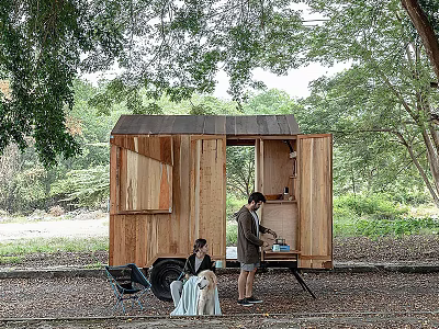 Wooden Trailer Style Cabin Surrounded by Trees with Two People Resting Outside 3d model