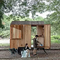 Wooden Trailer Style Cabin Surrounded by Trees with Two People Resting Outside