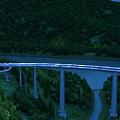 Elevated Bridge With Evening Lights Over River In Green Mountain Forest With Concrete Piers
