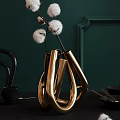 Golden Metallic Vase With Unique Loop Design Holding White Cotton Branches Against Dark Green Wall