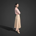 Woman in pink top and beige long skirt with crossed arms standing against gray background