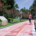 Park Landscape With Red Running Track Number Markers Pink Trees Green Grass And Clear Sky