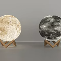 Two Moon Lamps Featuring Lunar Surface Texture And Wooden Triangle Stand In Light Dark Shades