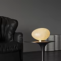 Oval Shaped Cream Colored Table Lamp with Gold Base on Black Table Near Leather Sofa