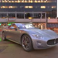 Silver Maserati Sports Car Parked On City Street With Lit Tall Buildings