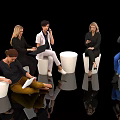Group of people sitting on white stools against black background using laptops phones and documents