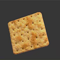 Golden square cracker with small holes and orange spots showing surface texture on gray background