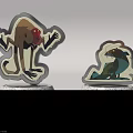 Two Cute Monster Themed Figurine Badges With Statuette Bases Inscribed Monster