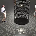 Two People Observing Black Cylindrical Structure With Surrounding Text And Light 3d model