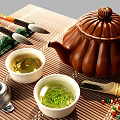 Traditional Tea Set With White Teacups Green Tea Leaves And Brown Teapot On Bamboo Mat