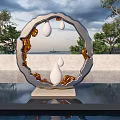 Circular Sculpture With White Teardrop Elements And Golden Accents On Reflective Water