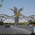 Modern Entrance Gate With Leaf Shaped Metallic Structure Loden Sign Surrounding Trees Vehicles And Pedestrians