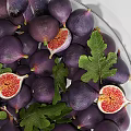Fresh Purple Figs in Glass Bowl with Golden Stand and Sliced Fruits with Green Leaves