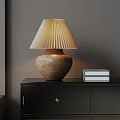 Pleated Beige Table Lamp On Black Cabinet With Stack Of Books