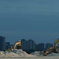 Heavy Duty Excavators Working on Sand Piles with Urban Skyline in Background