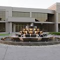 Multi Tiered Water Fountain In Front Of Modern Building With Glass Windows And Green Shrubs