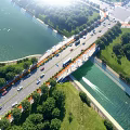 Aerial View Of Urban Road Bridge With Vehicles Over Waterway And Lush Green Areas