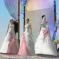 Three Women In White Pink Wedding Dresses Standing Before Colorful Decorated Arch With Clothing
