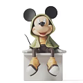 Mickey Mouse Sculpture Wearing Green Hoodie Yellow Top Brown Pants On White Platform