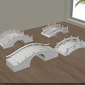 White Arched Stone Like Bridge Models Displayed on Wooden Floor with Window and Plant