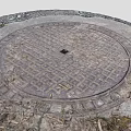 Circular Metal Manhole Cover On Stone Base With Surrounding Weeds And Small Stones