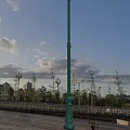 Outdoor Street Lamp Under Blue Sky With Clouds Trees Railings And Distant Buildings