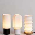 Three Different Shaped Table Lamps With White Shades And Colored Bases On Light Wall