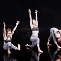 Three Women Performing Various Dance Poses In Activewear On Black Background With Floor Reflections
