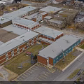 Aerial View Of Multiple Brick And Metal Buildings With Gray Roofs And Parking Lot