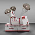 Gift Boxes With Metallic Parachutes And Red Bows On Chanel Display Base