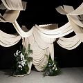 Stylish Floral Display Featuring White Draped Fabric And Central Decorative Greenery On Gray Floor