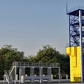 Industrial Training Tower With Blue Yellow Metal Structure Stairs Platforms And Surrounding Trees