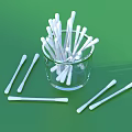 White Cotton Swabs in Transparent Glass Cup and Scattered on Green Background