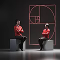 Two Women Wearing Red Blouses Sitting On Gray Cubes With Red Geometric Design